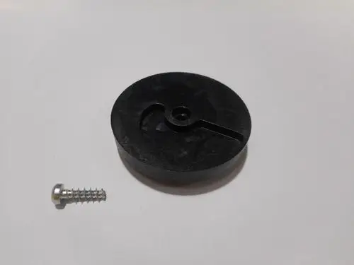 Schwarze Kupplung von Remeha mit einem Schlitz und einer zentralen Bohrung, daneben eine silberne Schraube mitGewinde.